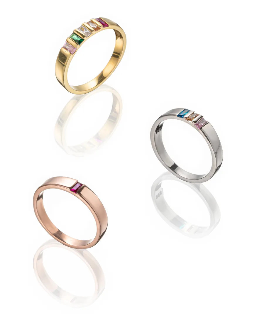 Altın, gümüş ve rose gold renk taşlı üç yüzük, beyaz fonda yansımalı